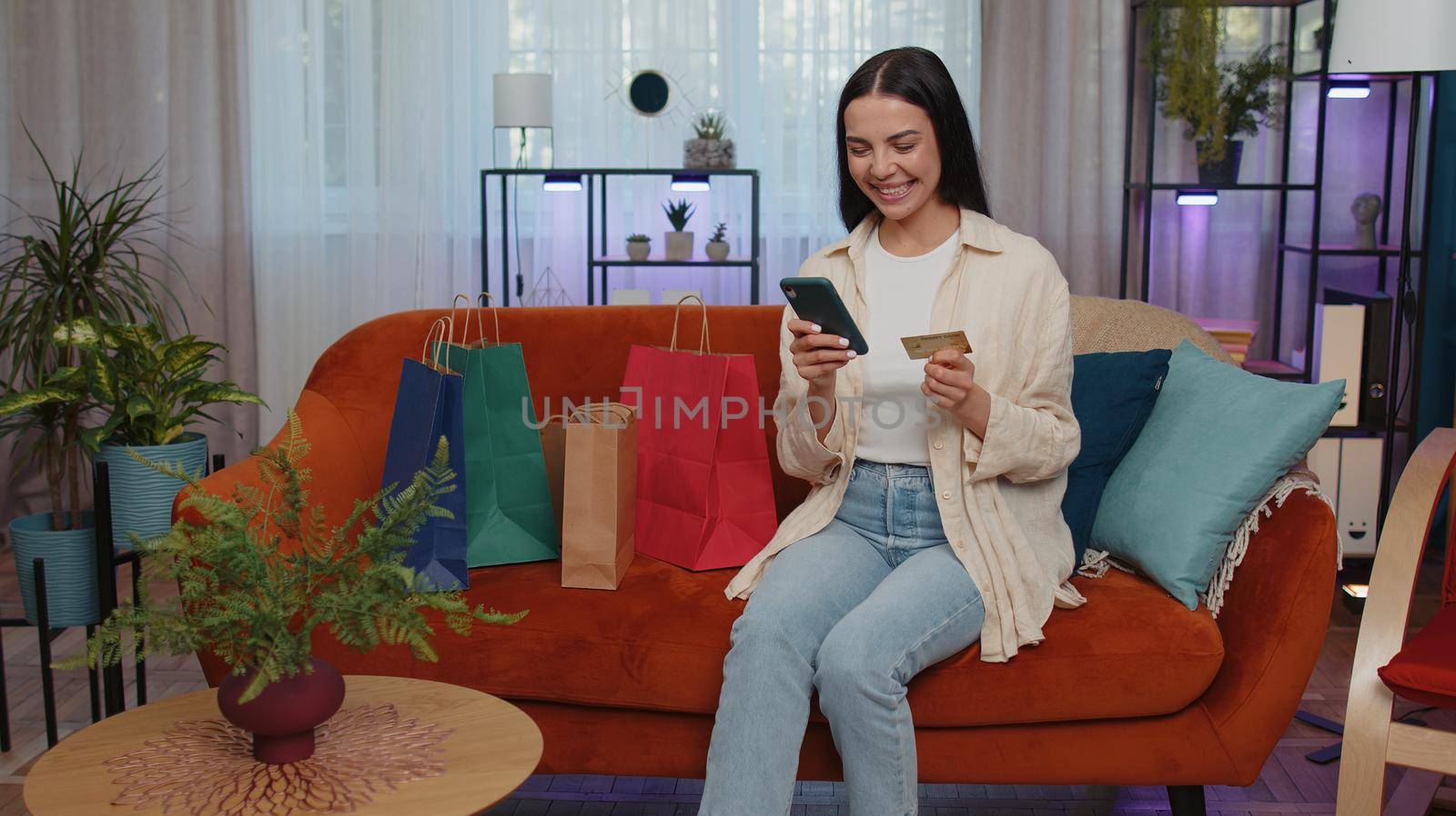Happy shopaholic young woman sitting with shopping bags making online payment with credit card by efuror