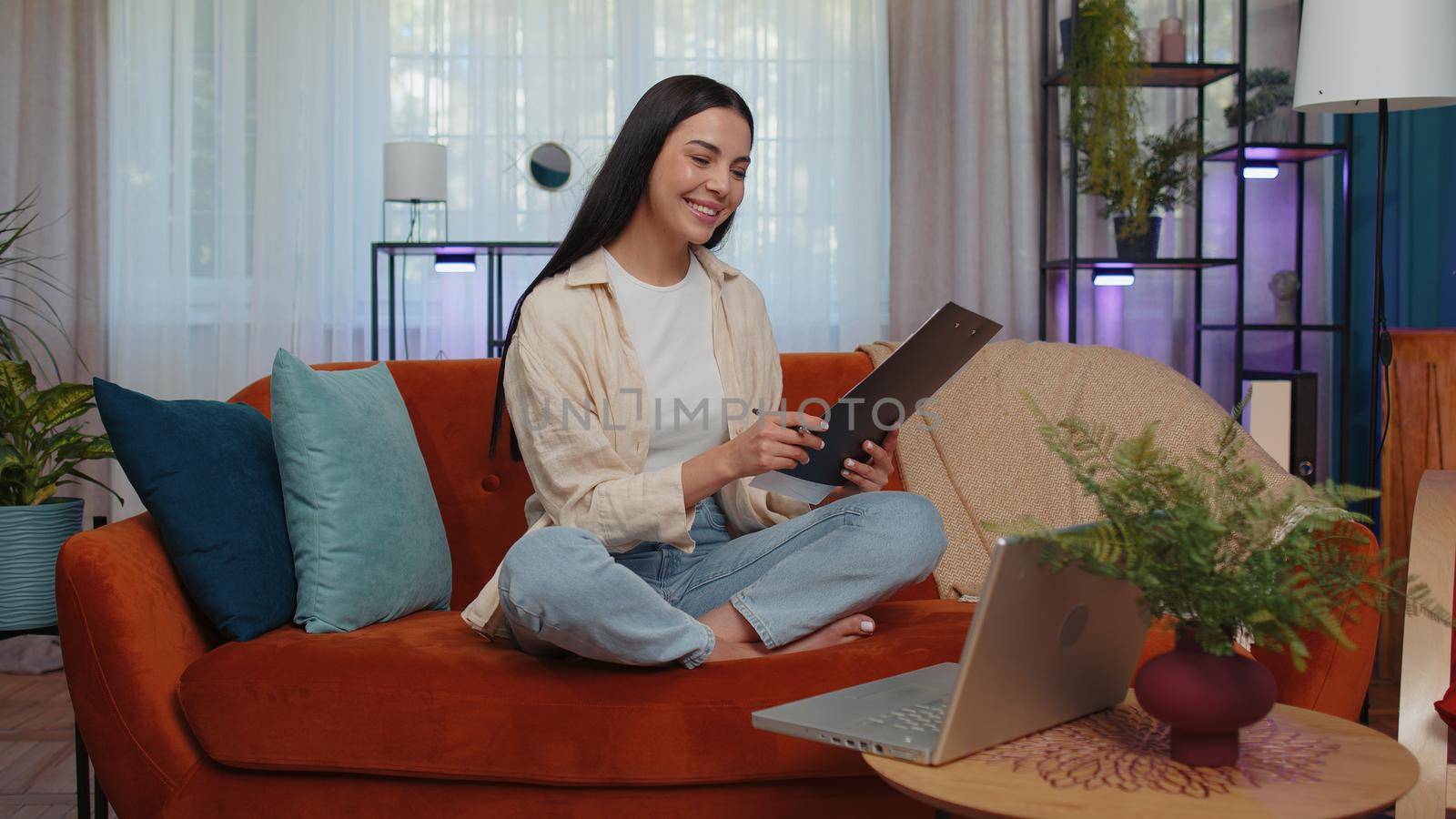 Girl accountant working with financial graph documents, calculate taxes for charts and graph reports of home income on couch. Young businesswoman working on laptop computer, planning expenses budget