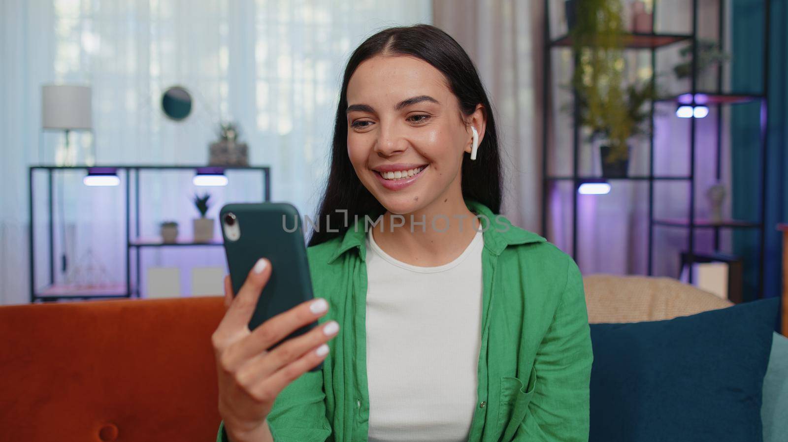 Portrait of caucasian girl blogger influencer making phone conversation call with social media followers sitting on couch at home in room. Happy excited woman enjoying mobile loudspeaker vlog talking