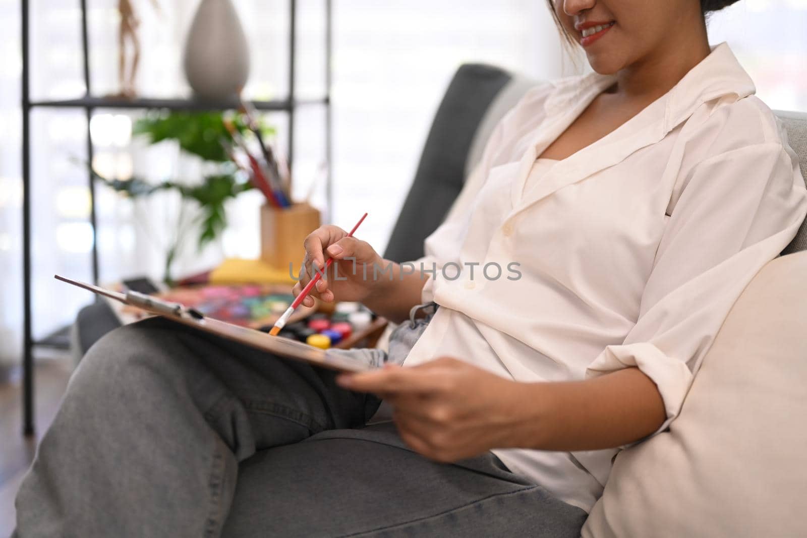 Relaxed young woman sitting on couch and painting picture with watercolor. Art, creative hobby and leisure activity concept.