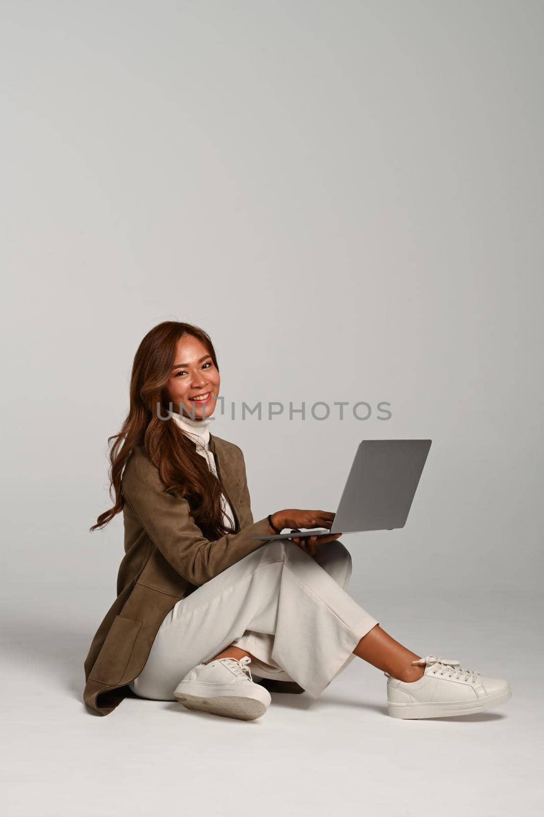 Attractive woman in in fashionable autumn clothes sitting with laptop on beige background.