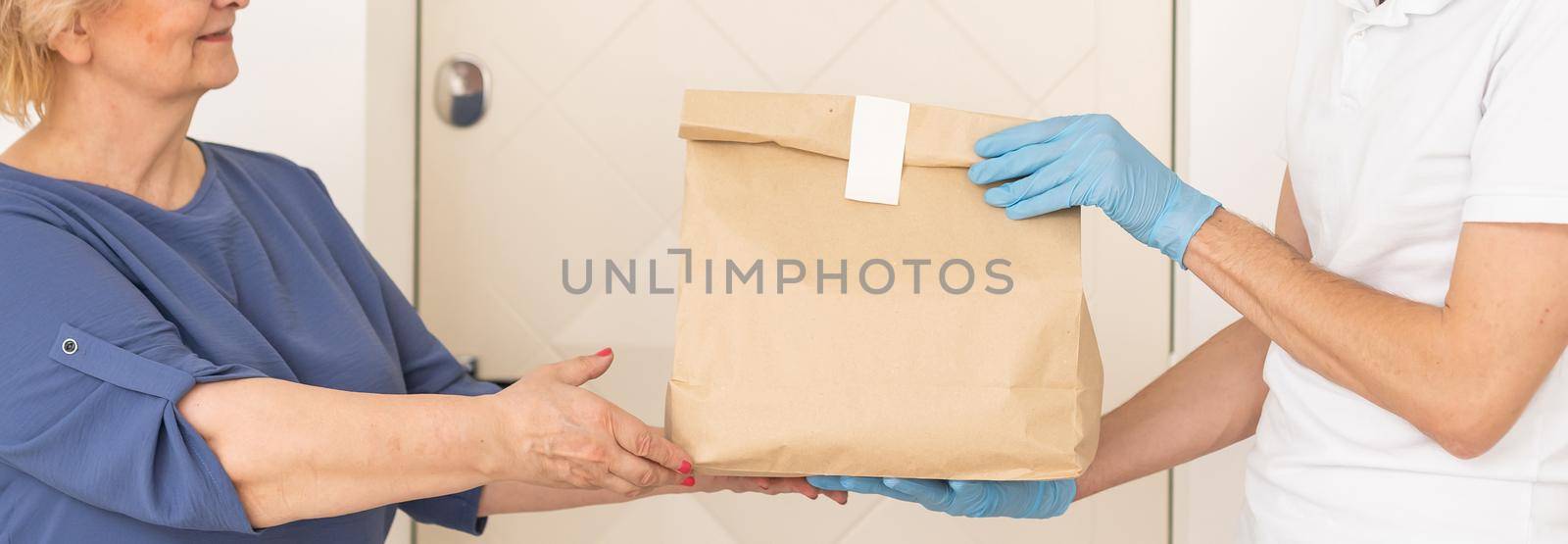 Courier of food delivery company giving products to elderly woman. Concept of epidemic.