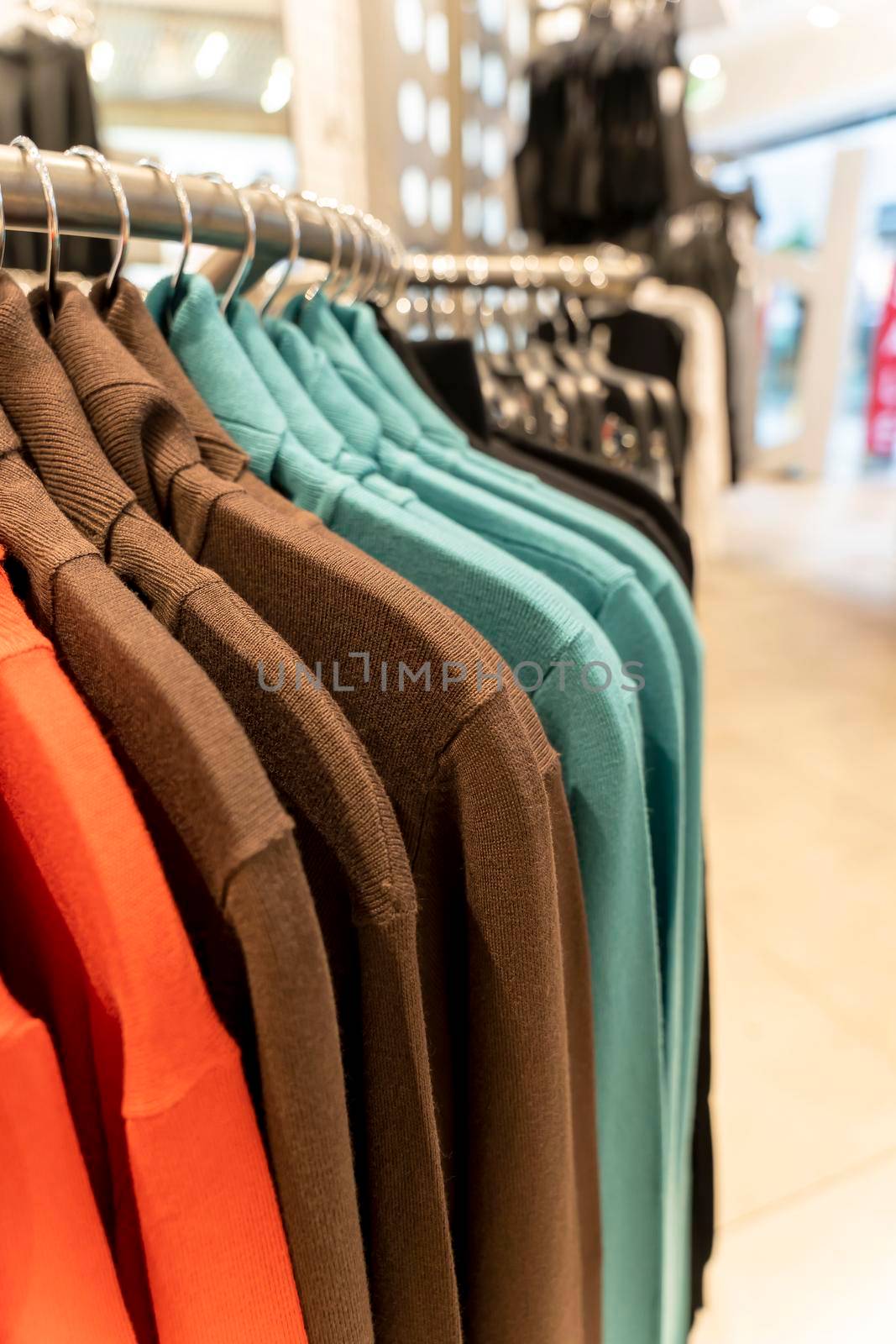 multi colored sweatshirts hang on a hanger in a clothing store. Close-up: Hangers with casual clothes in a mall. Designer clothing collection. New collection in fashion boutique. vertical photo
