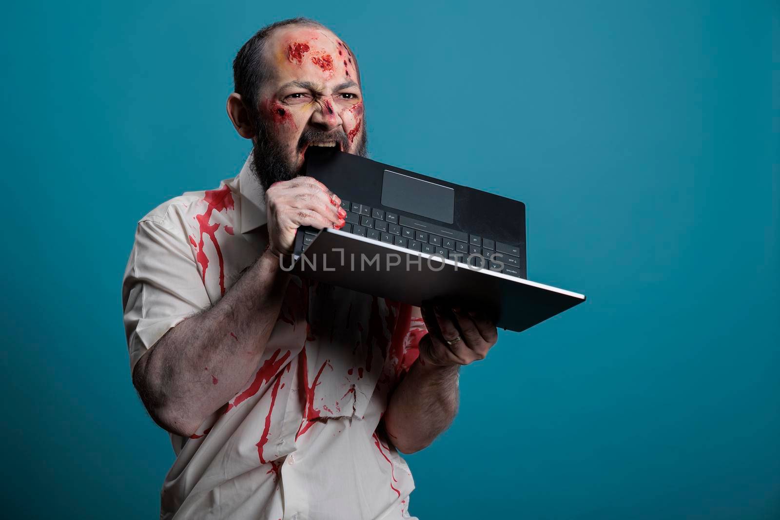 Spooky halloween zombie biting on laptop computer by DCStudio