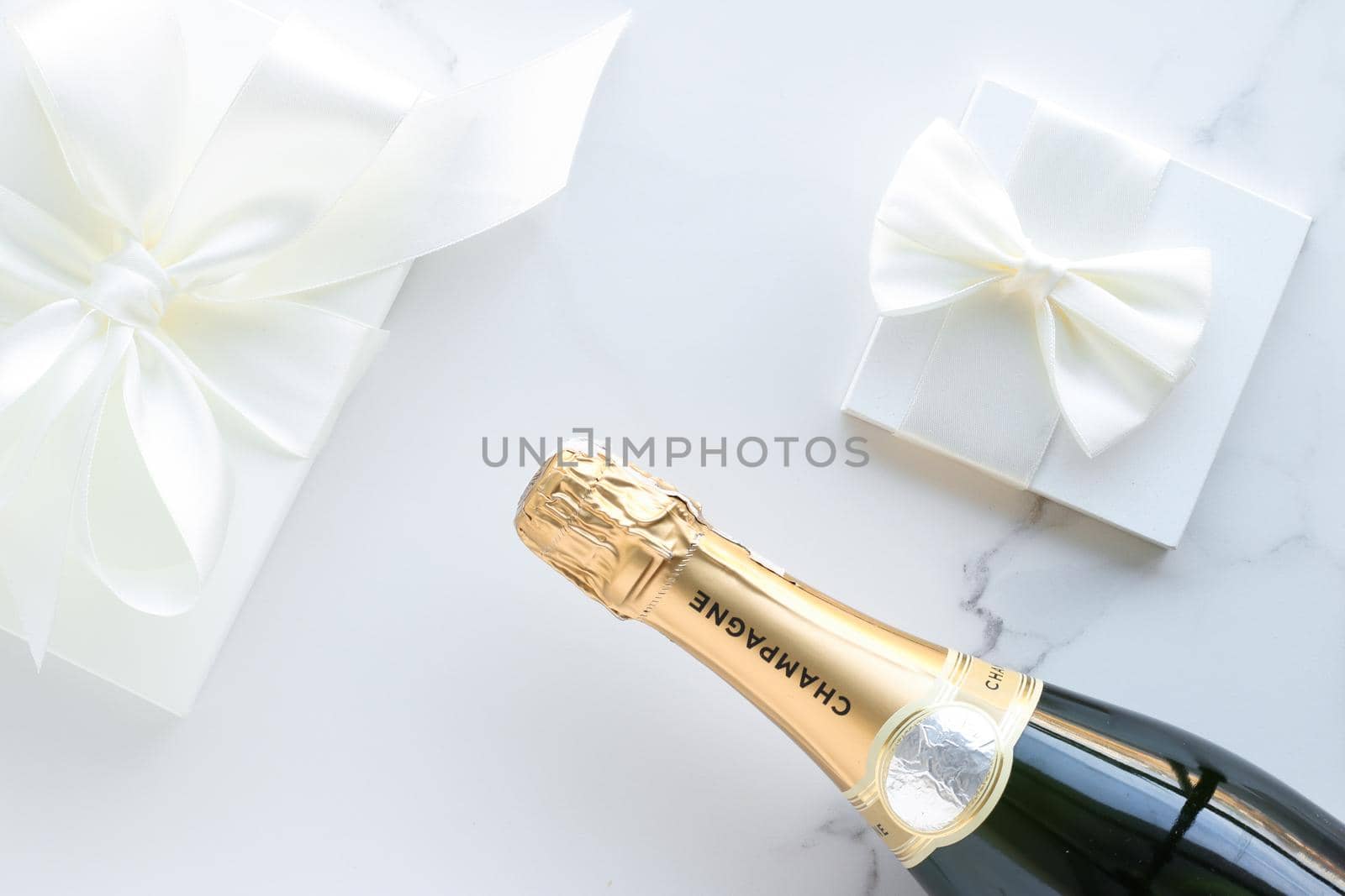 A champagne bottle and a gift box on marble by Anneleven