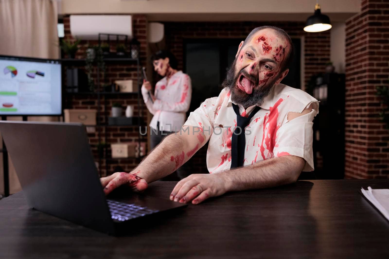 Creepy scary zombie using laptop at desk by DCStudio