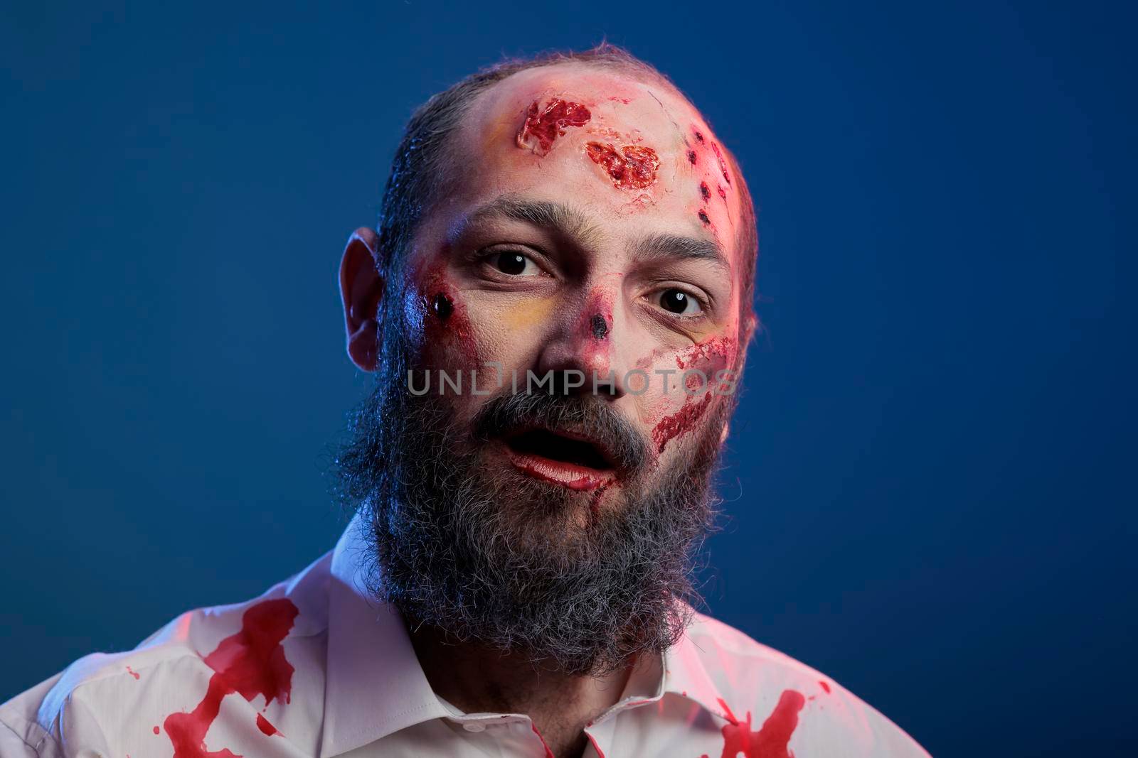 Portrait of undead scary zombie man posing with bloody scars and spooky halloween costume looking dangerous and apocalyptic. Horror aggressive deadly monster corpse eating brain.