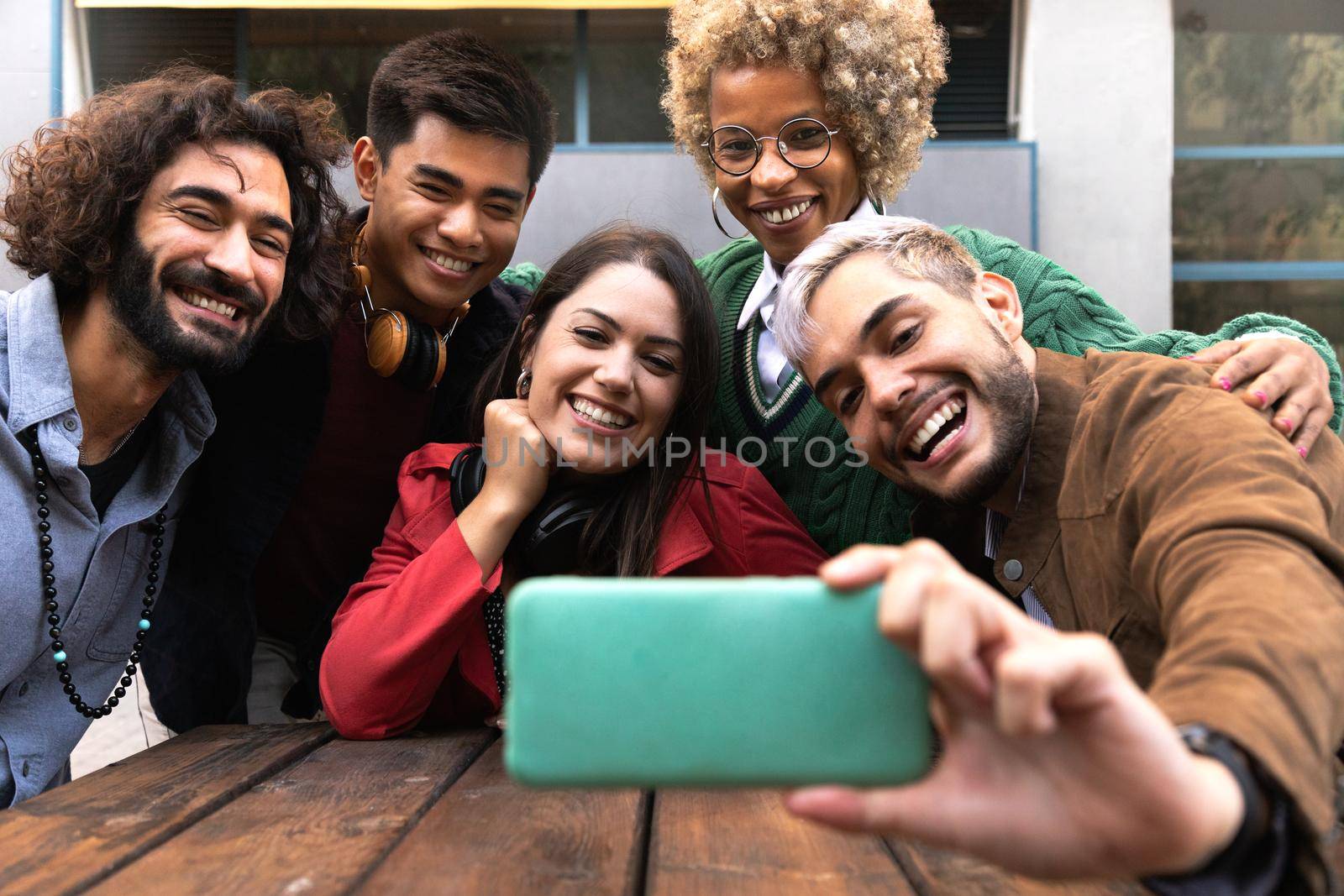 Smiling multiracial young friends take selfie together with mobile phone outdoors.Technology and friendship concept.