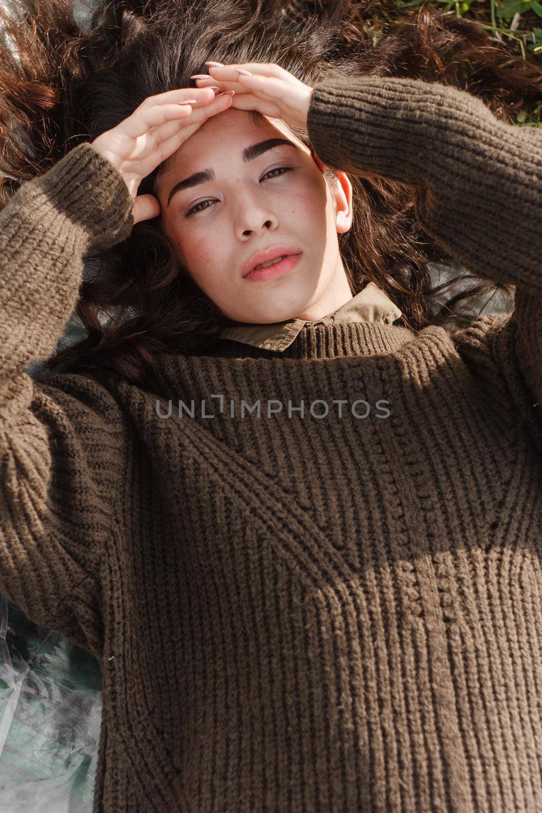 An Asian woman is lying on the ground in a field in a brown sweater. The concept of manufacturing clothing from recycled plastic. by Annu1tochka