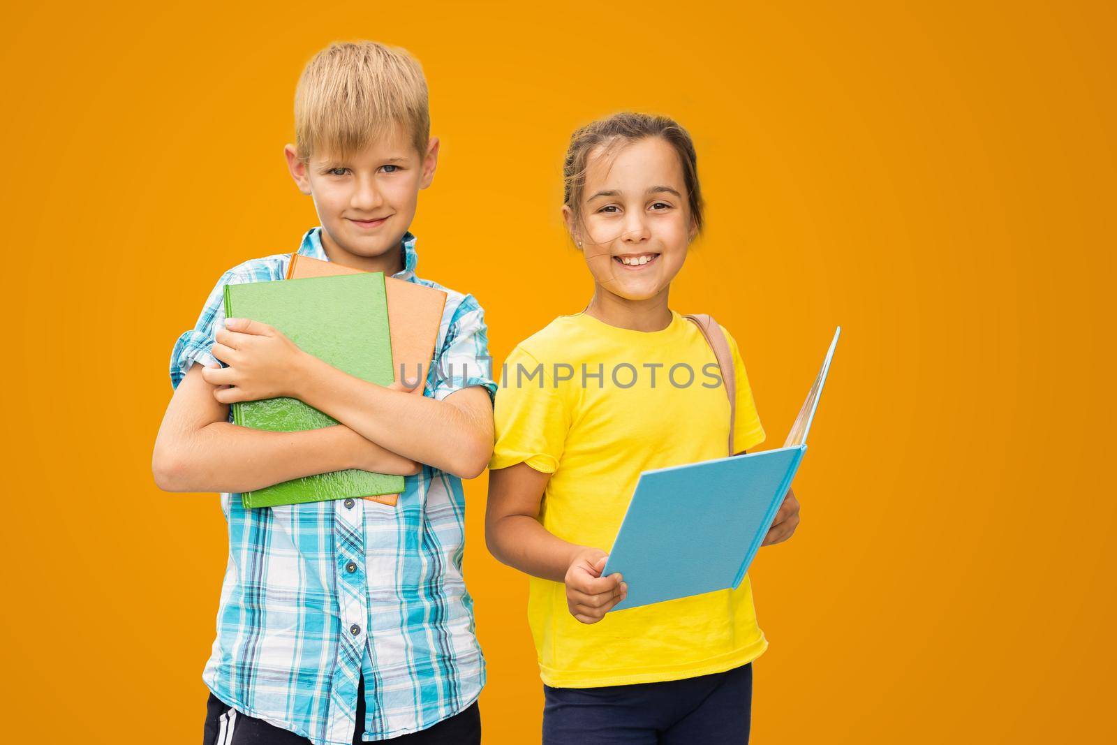 Photo of two small girl boy schoolchildren brother sister classmates hold books isolated orange color background.