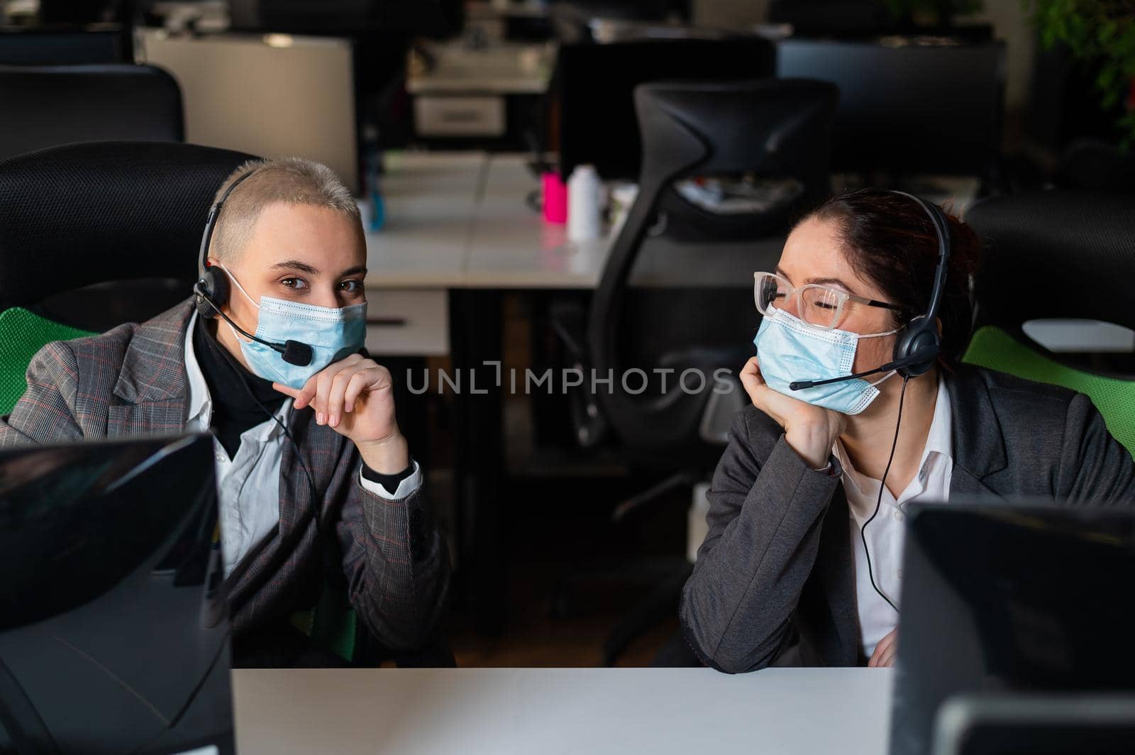 Two women in medical masks and headsets are working in the office.