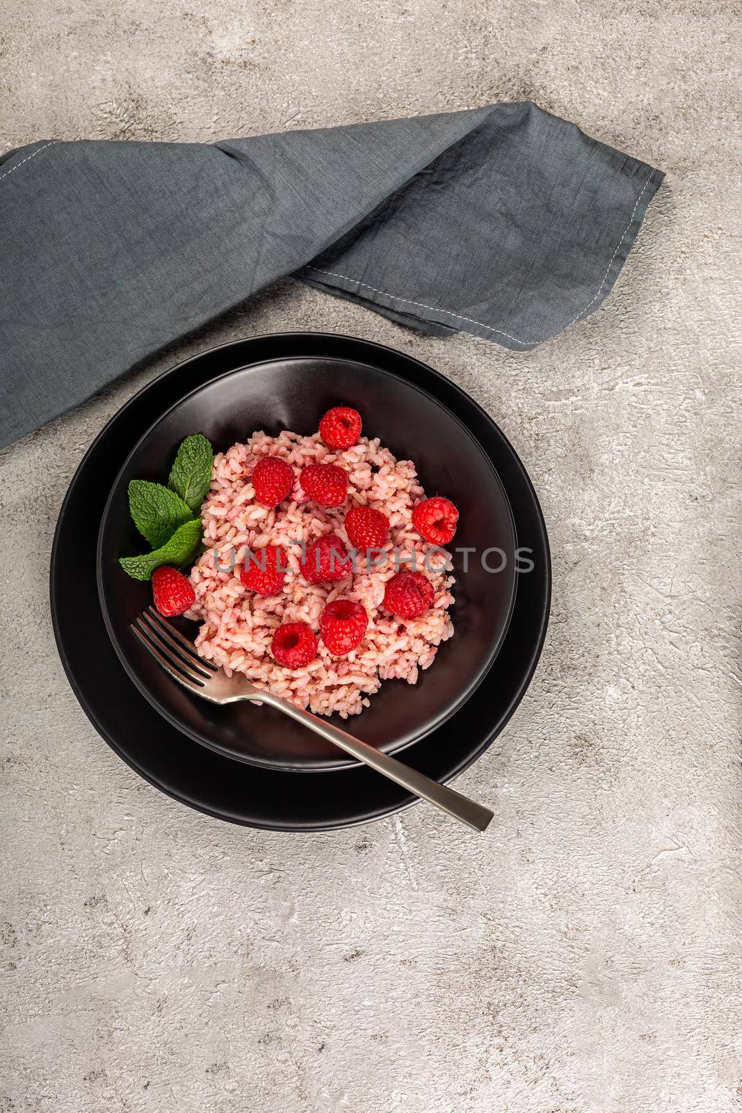 Healthy food on gray concrete background. Fresh raspberries risotto on a delicate and elegant dish