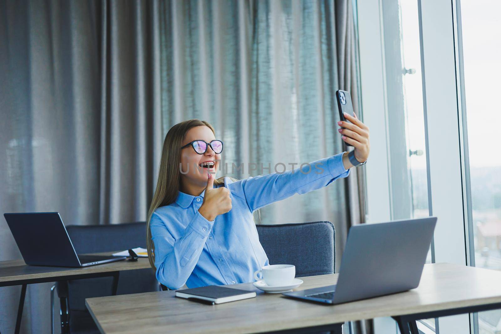 Smart female employee with netbook looking at camera during mobile call, successful freelancer in jacket talking on phone via app