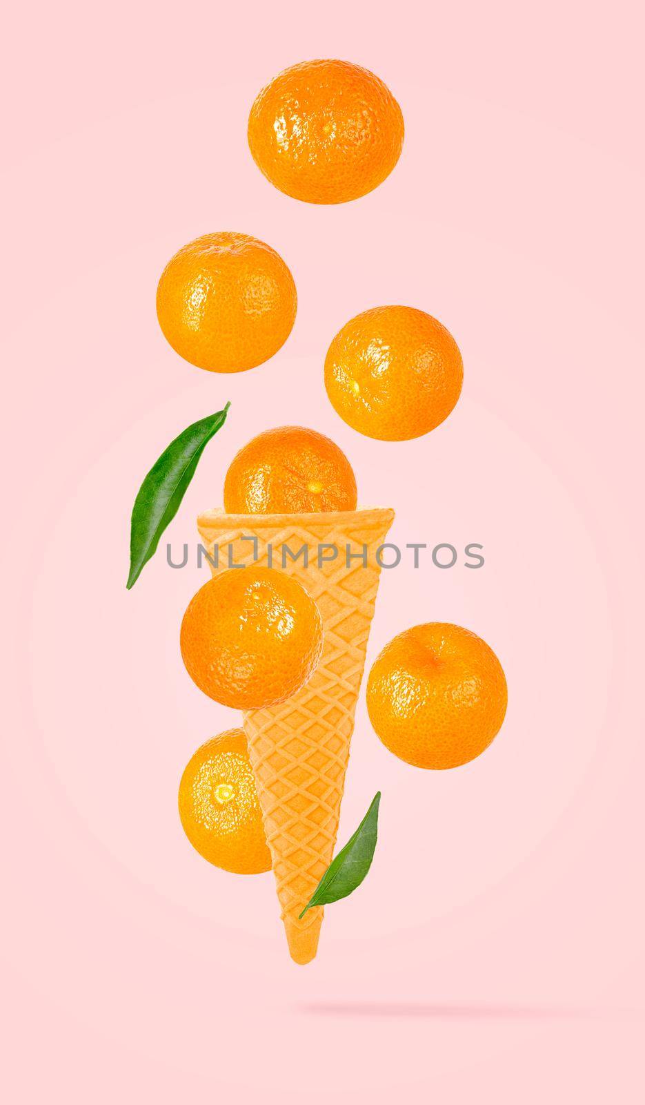 Isolated ice cream cone with fruits in the air. Seven falling whole tangerines on pastel pink background with clipping path as package design element and advertising. Full depth of field.