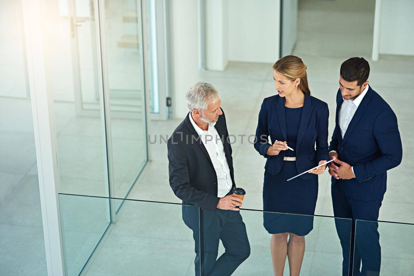 Their decisions take the company forward. three colleagues talking together over a digital tablet while standing in a modern office
