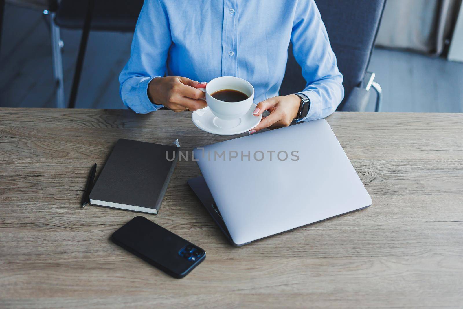 Portrait of cheerful woman in classic glasses smiling in free time in cafe with coffee, positive european woman in blue shirt, desk with laptop, remote work