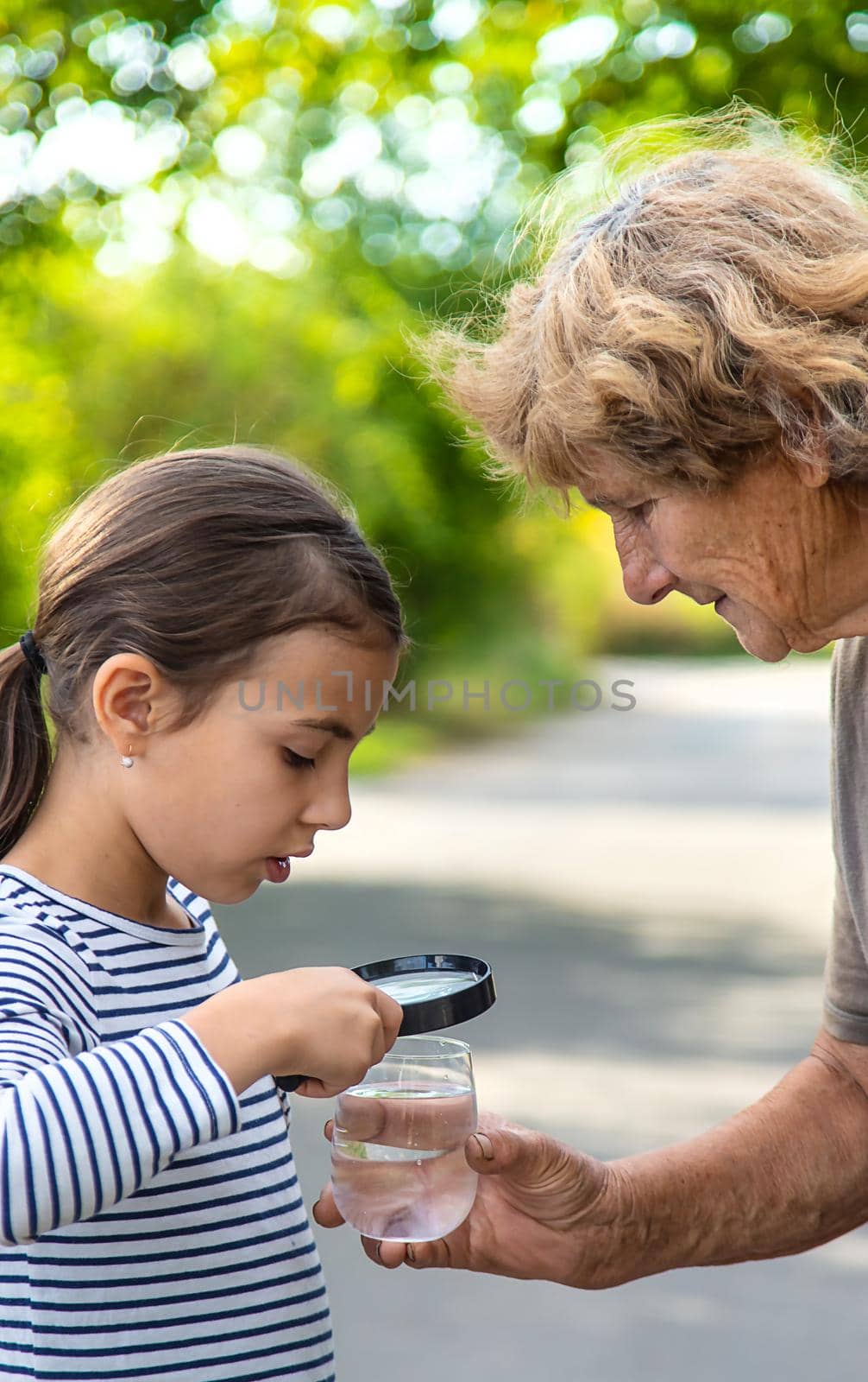 A child and grandmother examines the water with a magnifying glass. Selective focus. by yanadjana