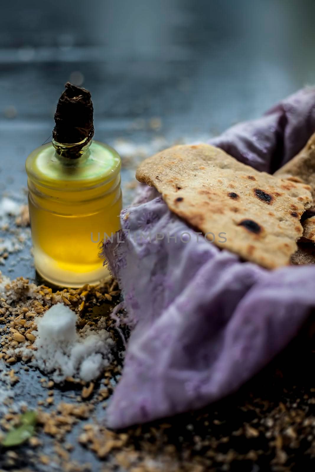 Shot of bhakri in a basket container along with some wheat flour spread on the surface and some cooking oil in a small glass bottle on a black colored surface. close up shot of traditional Gujarati bread Bhakri.