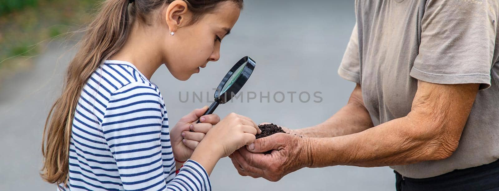 The child examines the soil with a magnifying glass. Selective focus. by yanadjana