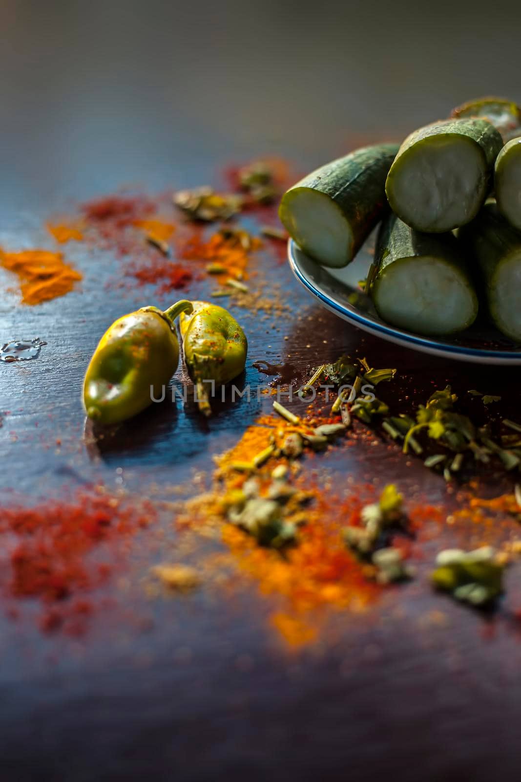 Close up shot of raw Galka or sponge gourd cut in a glass plate along with all the spices including Haldi, Mirchi,namak,garam masala, etc on a brown wooden table. Vertical high angle shot.