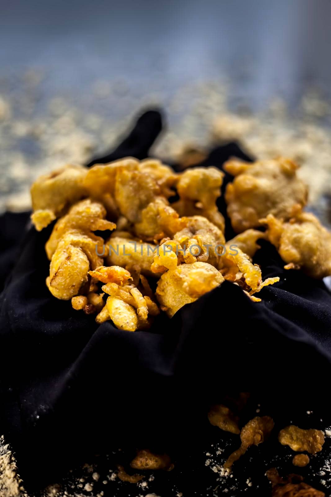 The famous shot of banana bhajia in a black colored container along with some raw banana and spices that are needed to make it.