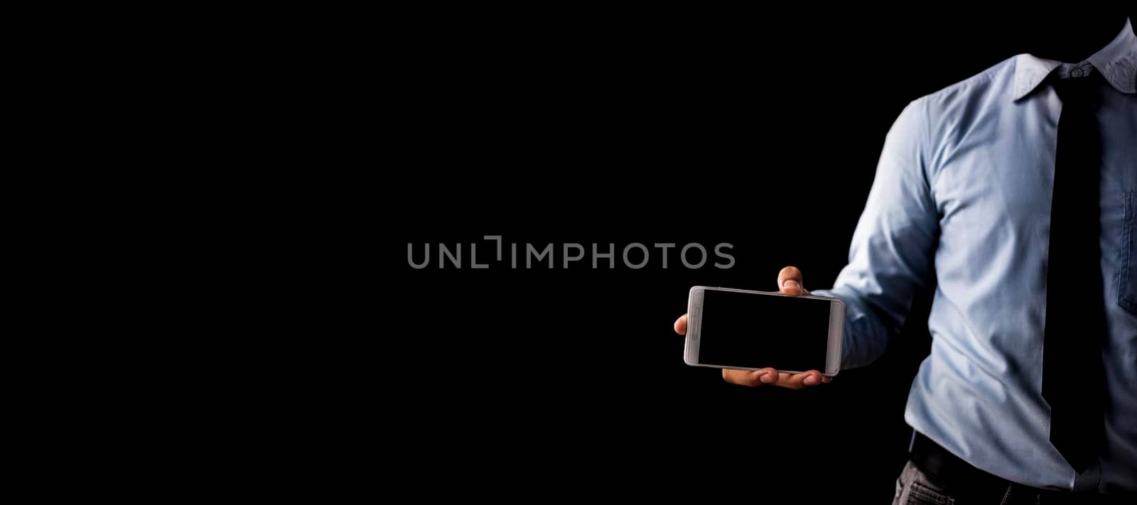Smart faceless businessman showing a practical display of his vision in his smartphone isolated on black background. by mirzamlk