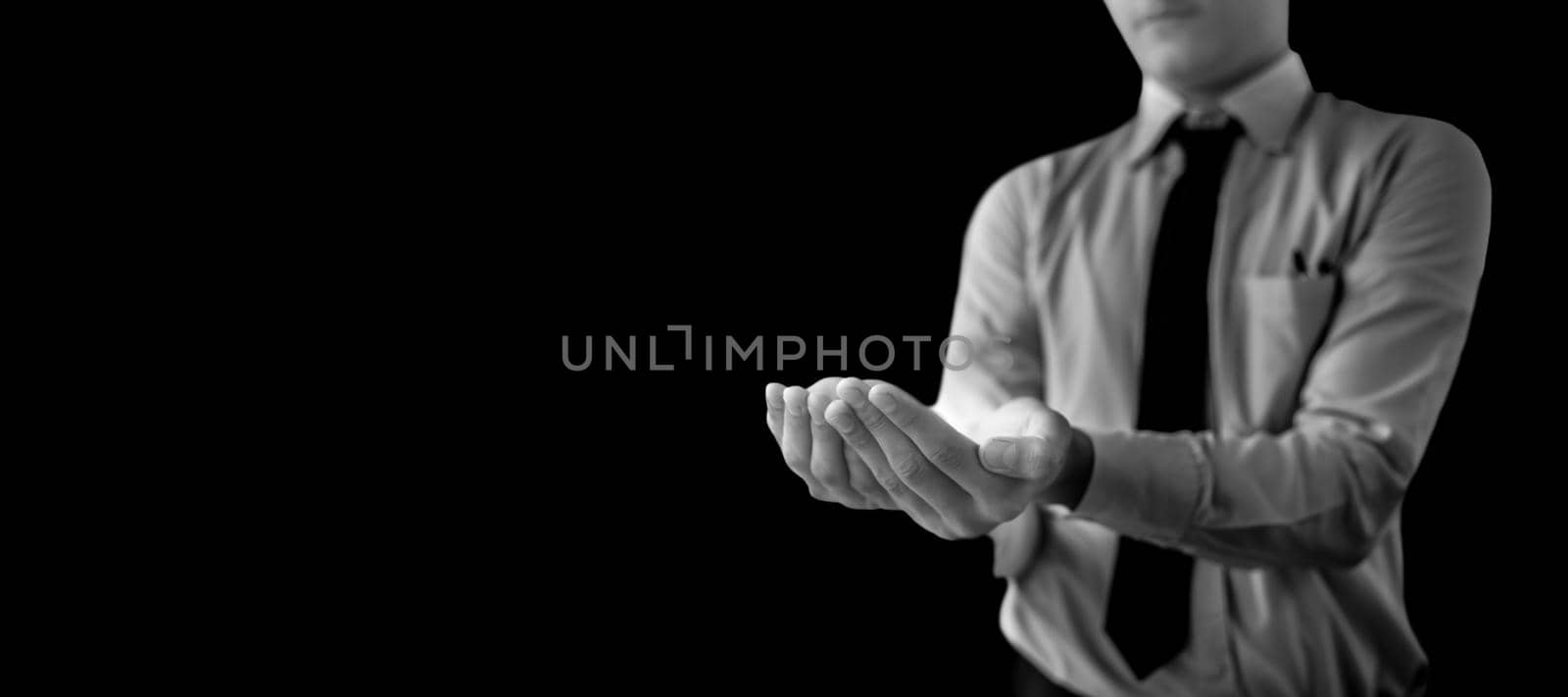 Shot of a unrecognizable man wearing blue shirt black tie and hands in a shape containing something inside it isolated on black background.