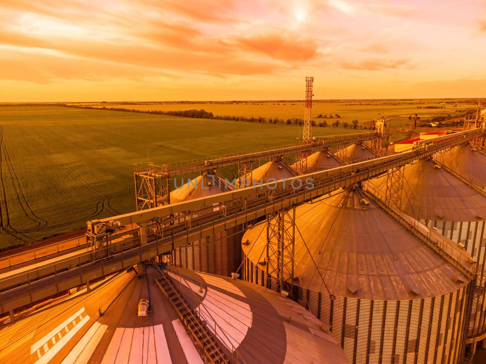 Grain elevator. Metal grain elevator in agricultural zone. Agriculture storage for harvest. Grain silos on green nature background. Exterior of agricultural factory