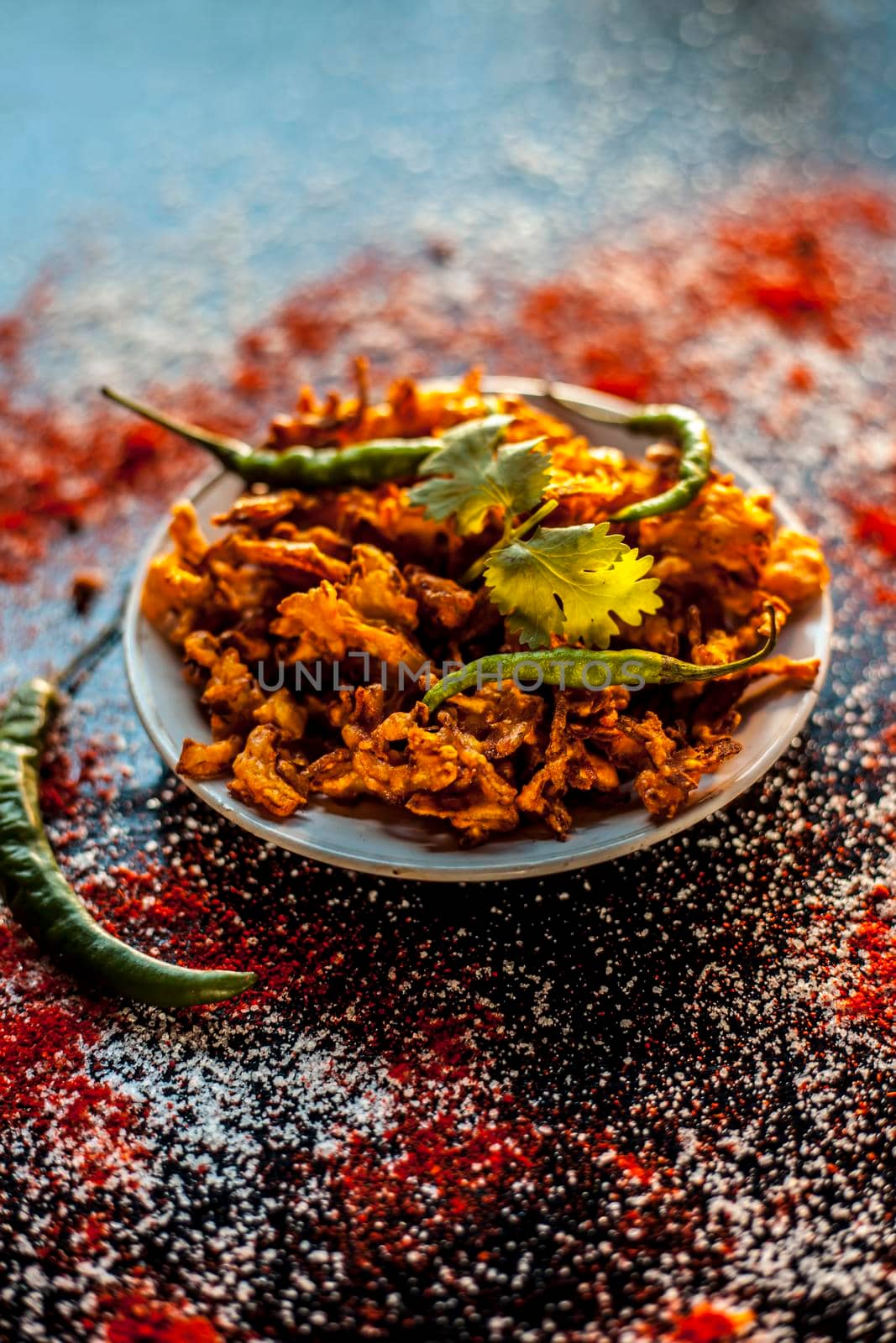 Shot of Piyaz pakora/bhaji/bhajji/bhajiya/bajji in a glass plate with some fresh green chilies and red chili powder along with it on black surface.