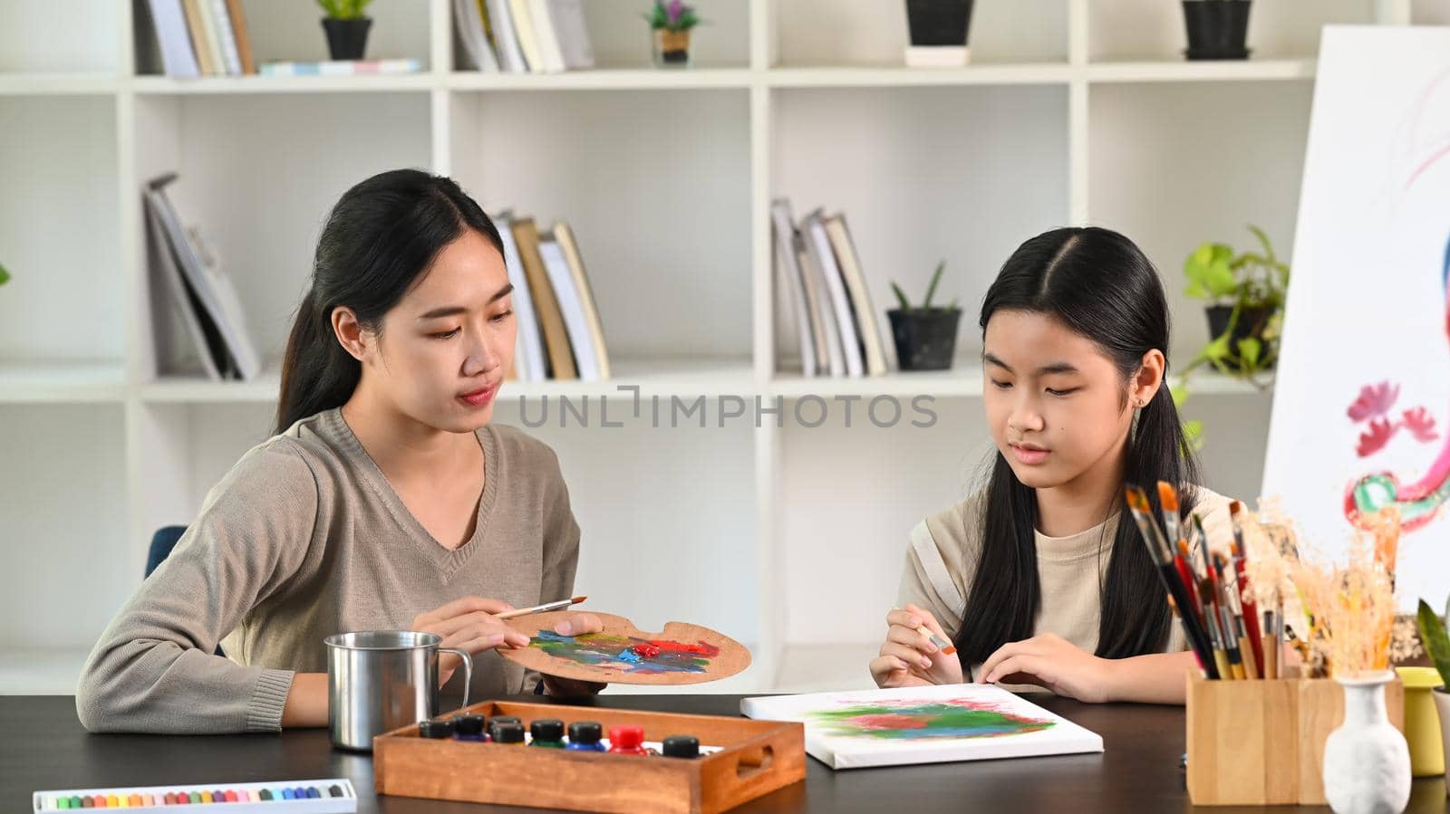 Beautiful asian mother and daughter painting together in living room.