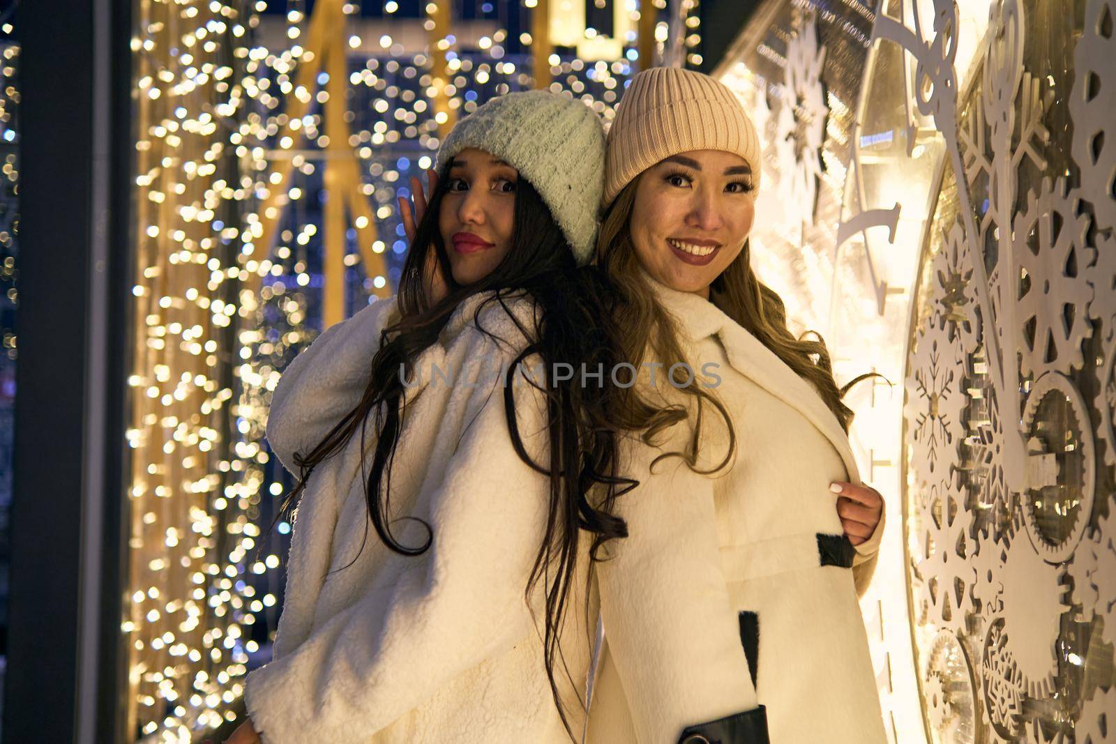 Two girlfriends asian girls in white coats are having fun hugging, new year, light bulbs