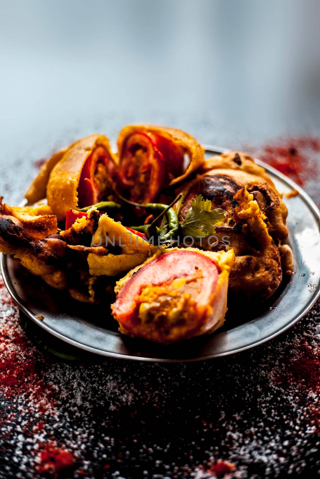 Shot of Indian tomato fritter on a glass plate along with some species on a black table. Shot of tomato pakora or tomato pakoda on a glass plate. by mirzamlk