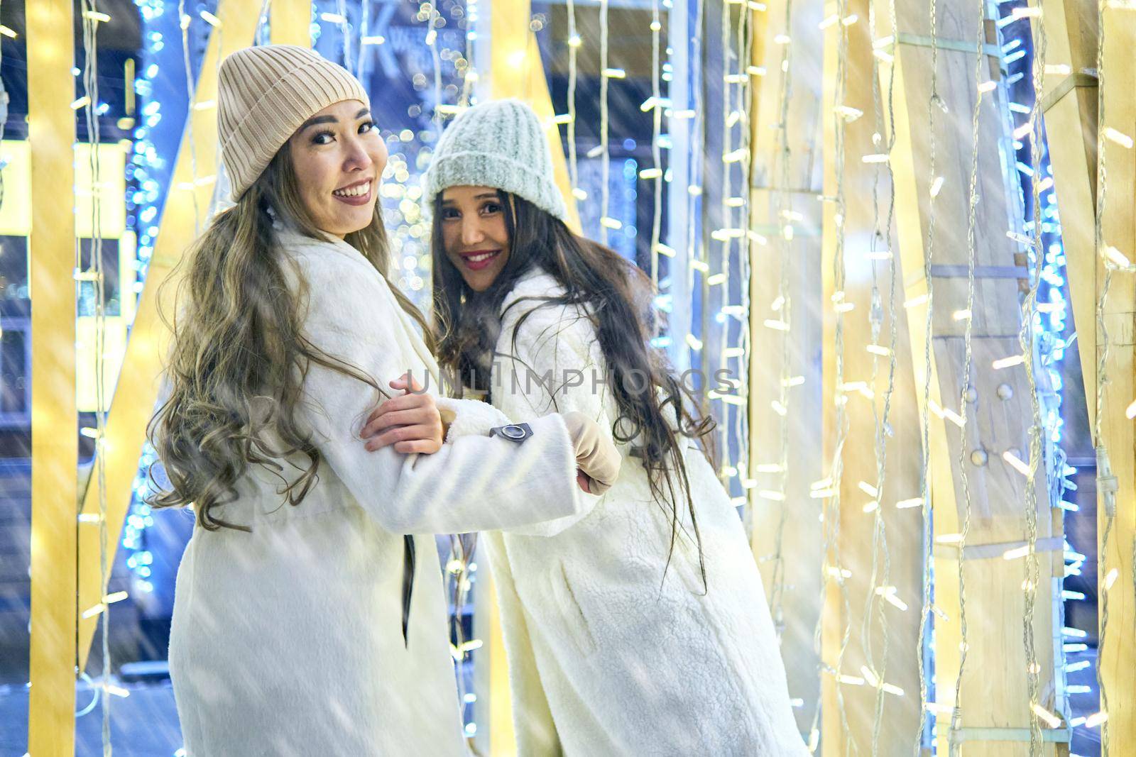 Two girlfriends asian girls in white coats are having fun hugging, new year, light bulbs