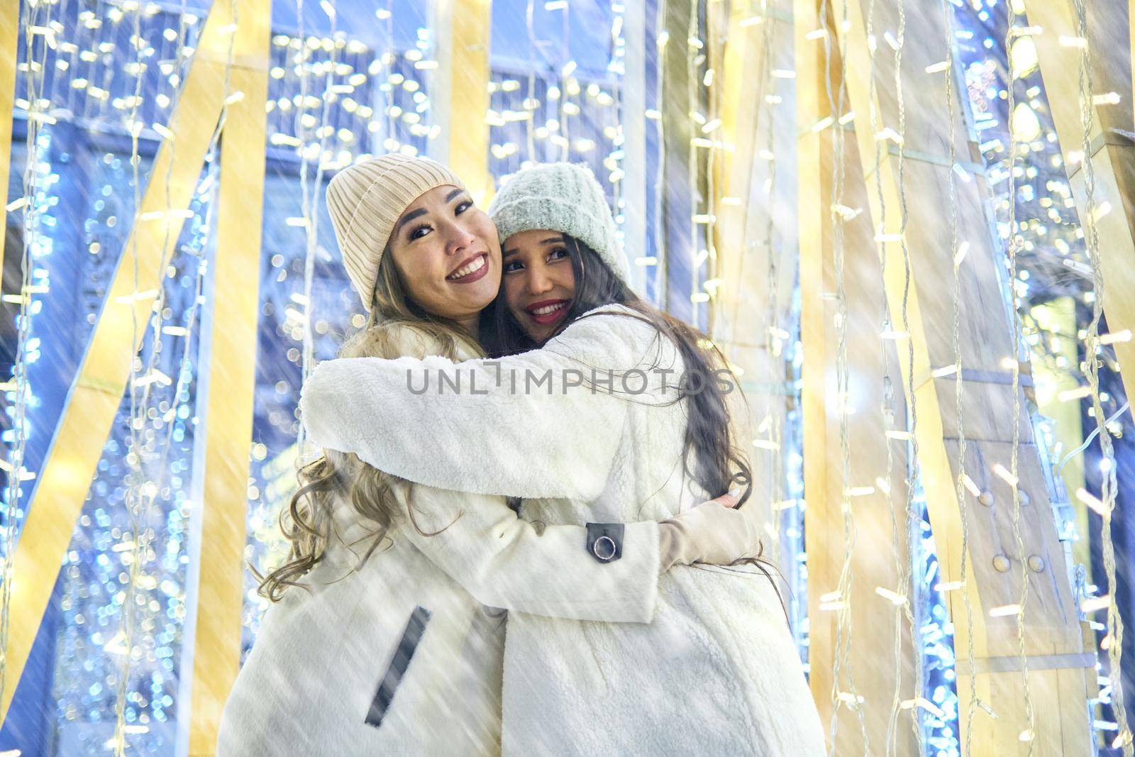 Two girlfriends asian girls in white coats are having fun hugging, new year, light bulbs