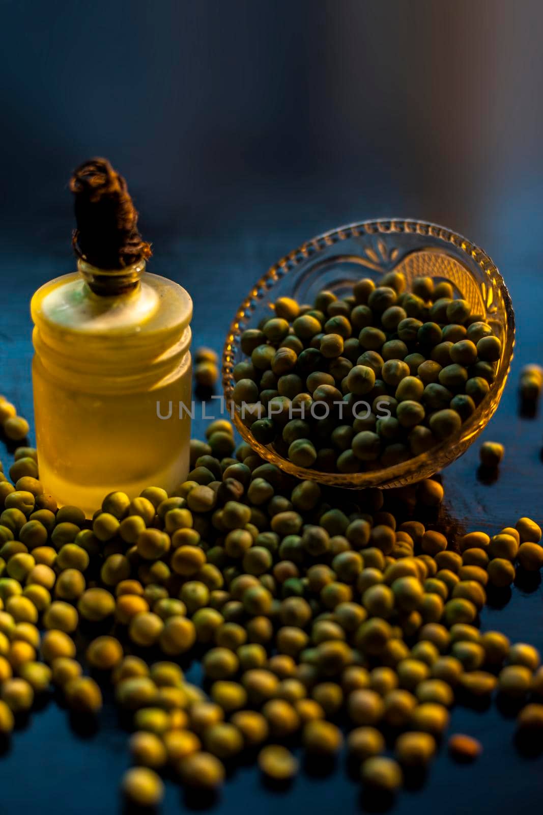 Shot of a bowl of green peas along with its extracted oil in a glass bottle on a black surface.