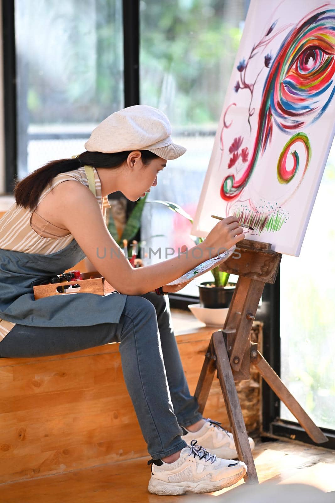 Female artist painting picture on easel in bright studio.