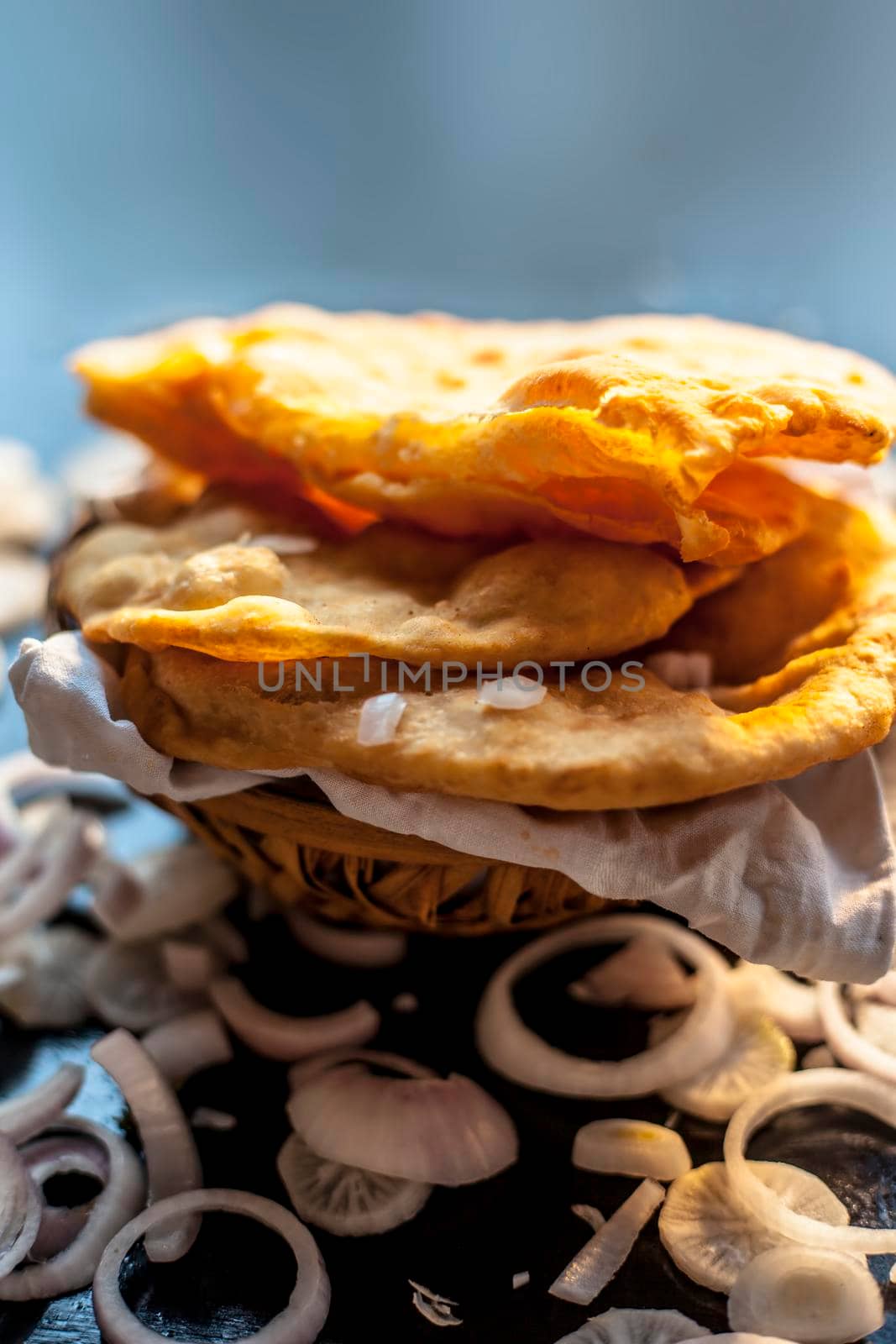 Close up shot of fresh fried bhatura or bhature or puri along with some cut onion rings on a black surface.