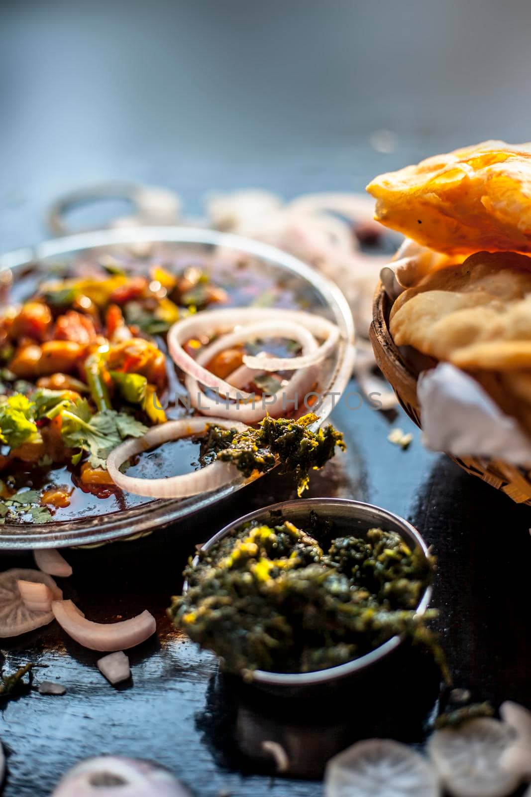 Full breakfast plate on the black surface. Indian Delhi style Chole bhature along with some onion rings and pudhina/mint chutney on a black surface.