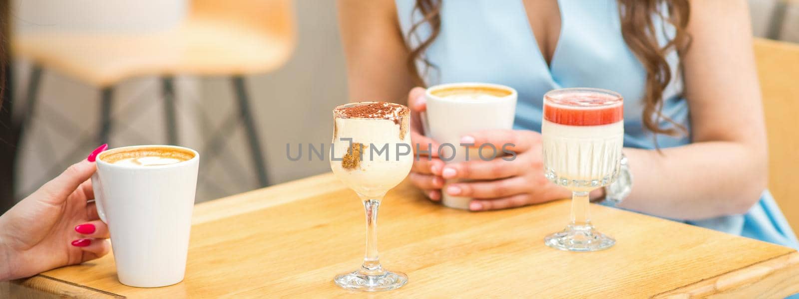 Hands of a young woman holding a cup of coffee with different cocktails on the table at the cafe