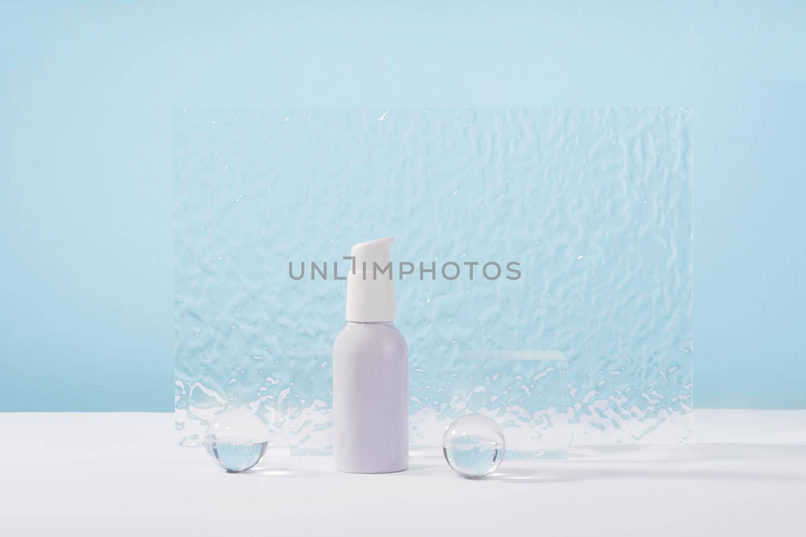 Cosmetic cream metallic pump bottle mockup on blue background with stylish props, glass balls and acrylic plate. Unbranded lotion white beauty product packaging. Product presentation by photolime