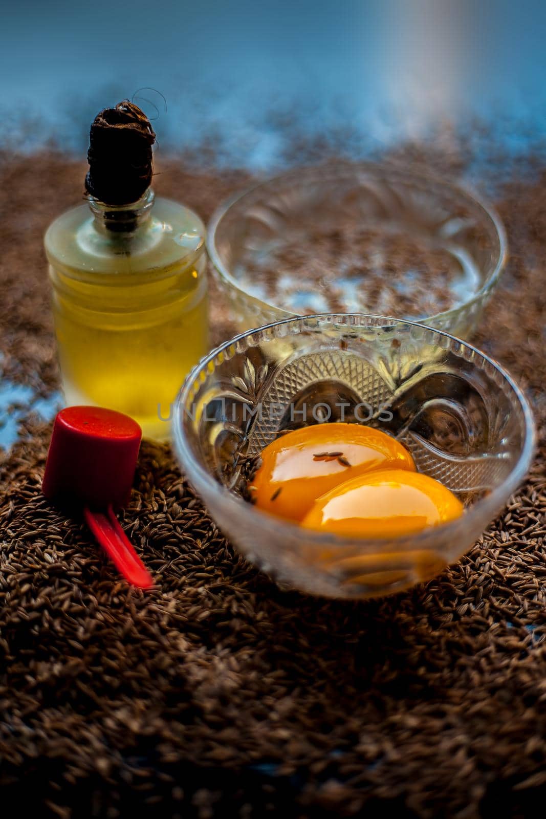 Hair mask for healthy long hair consisting of cumin seeds or zeera or jeera along with some raw egg yolk, water and some olive oil on a brown colored wooden surface.