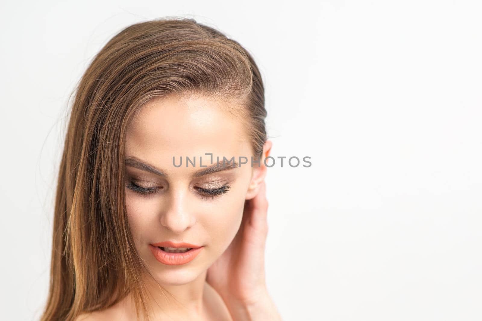 Beautiful young caucasian woman with natural makeup smiling and looking down standing on white background