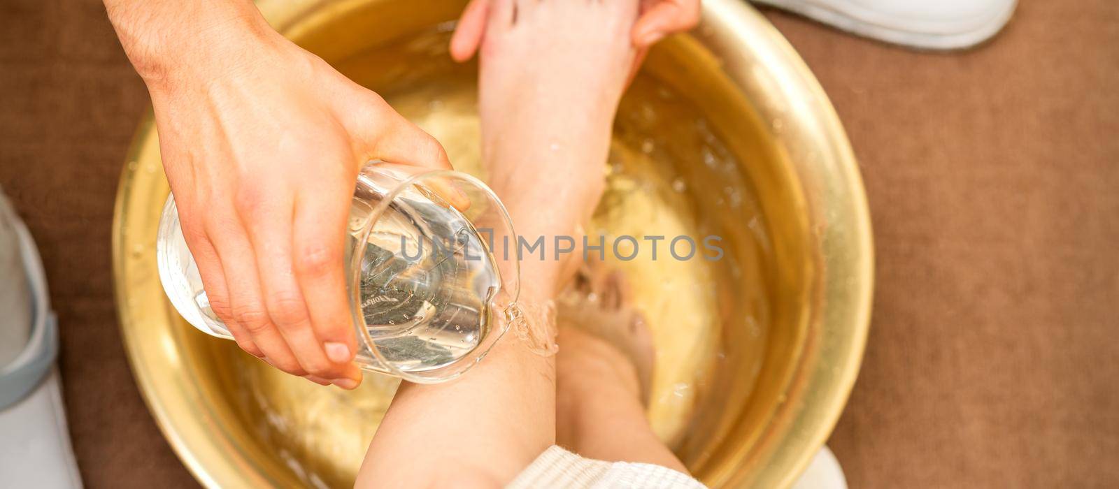 Top view of hands of masseur washing legs of a young woman in a golden bowl at beauty spa salon