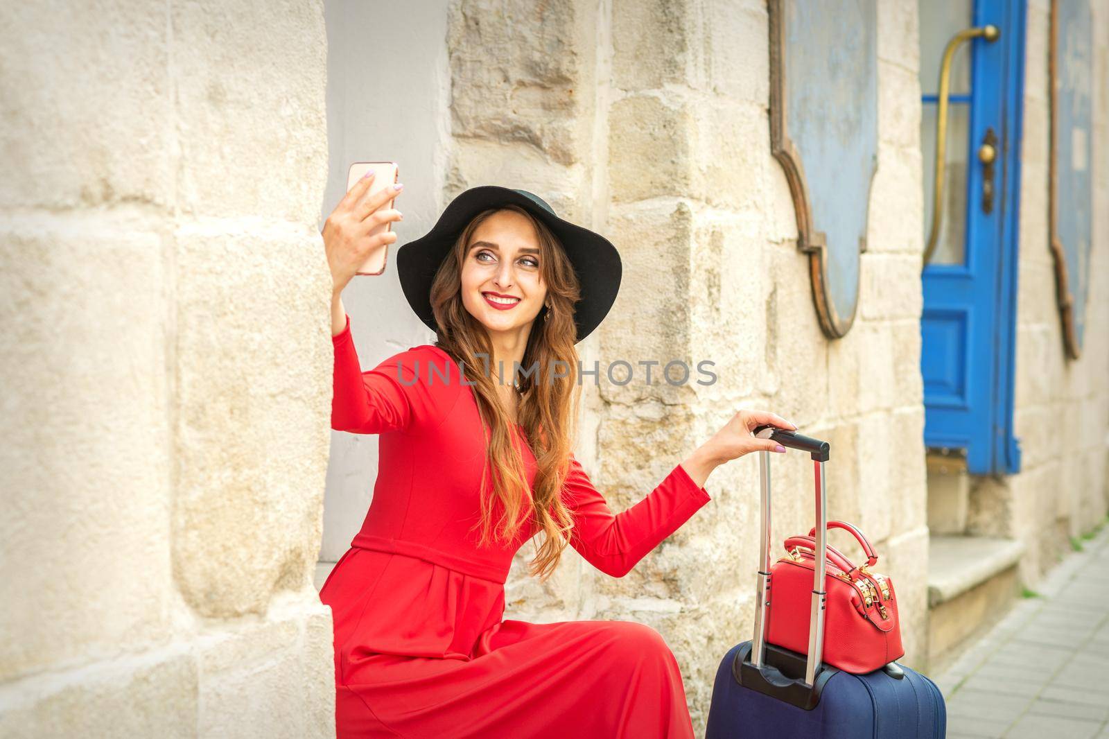 Beautiful young caucasian woman in black hat looking on the smartphone smiling and sitting on stairs at the door outdoors