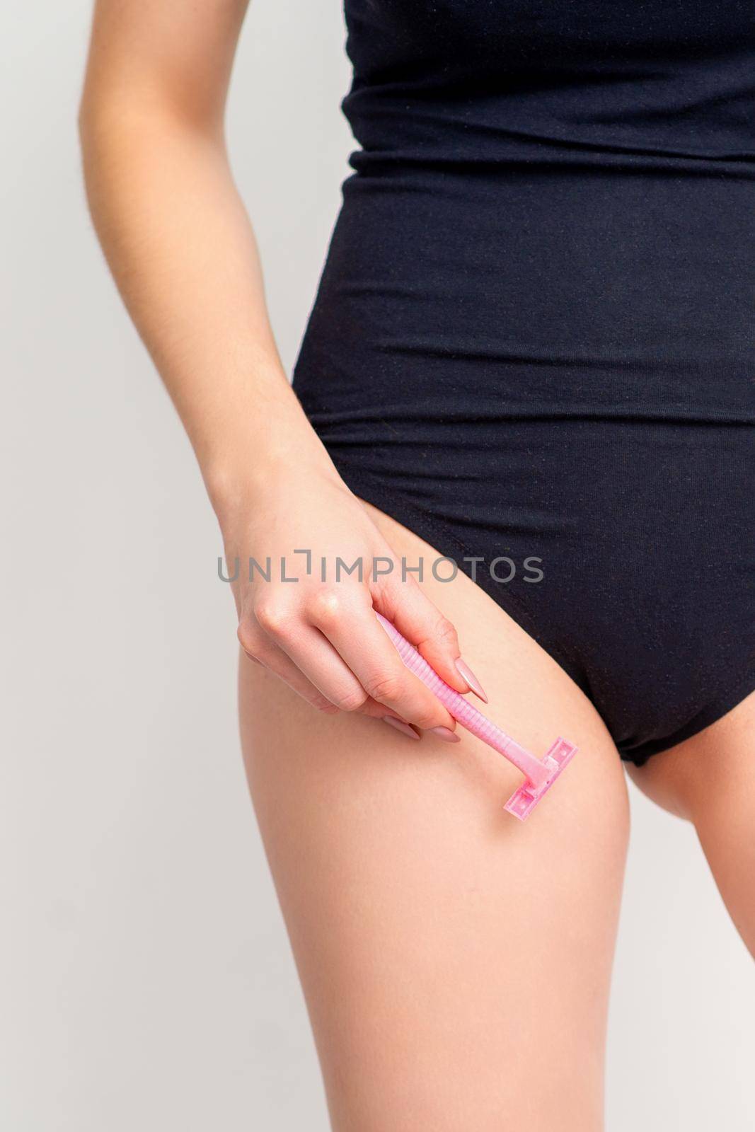 Young woman shaving crotch in bikini zone with two razors standing on white background, concept skincare and hair removal