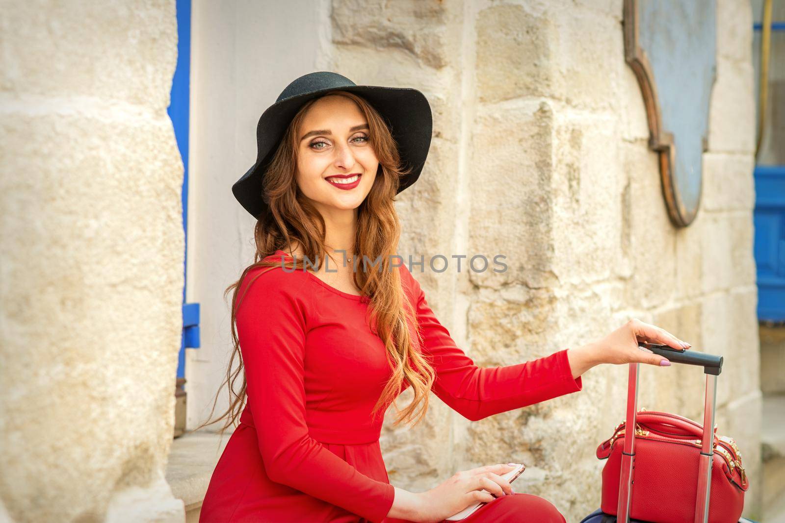 Beautiful young caucasian woman in black hat smiling and sitting on stairs at the door outdoors