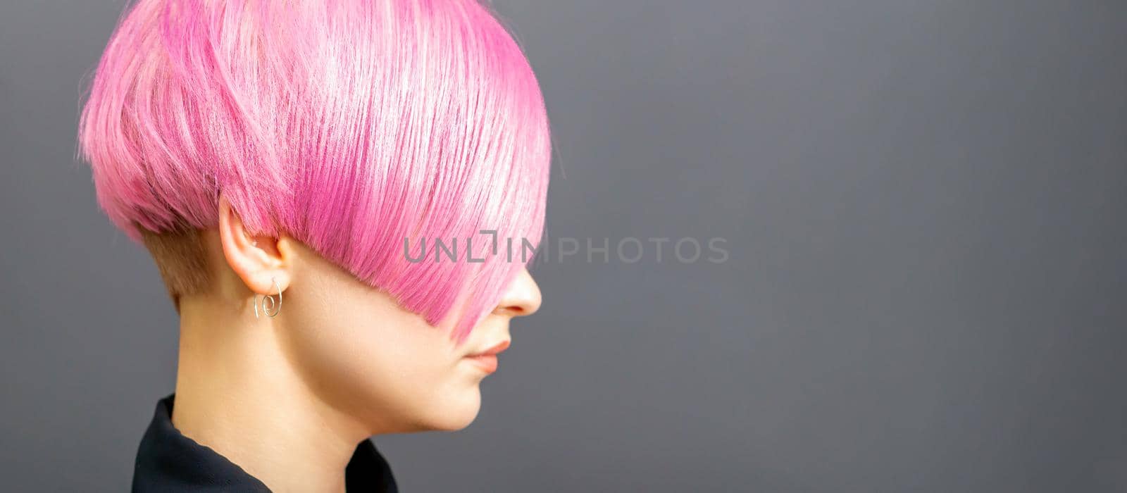 Profile portrait of a young caucasian woman with pink bob haircut isolated on a gray background, copy space. by okskukuruza