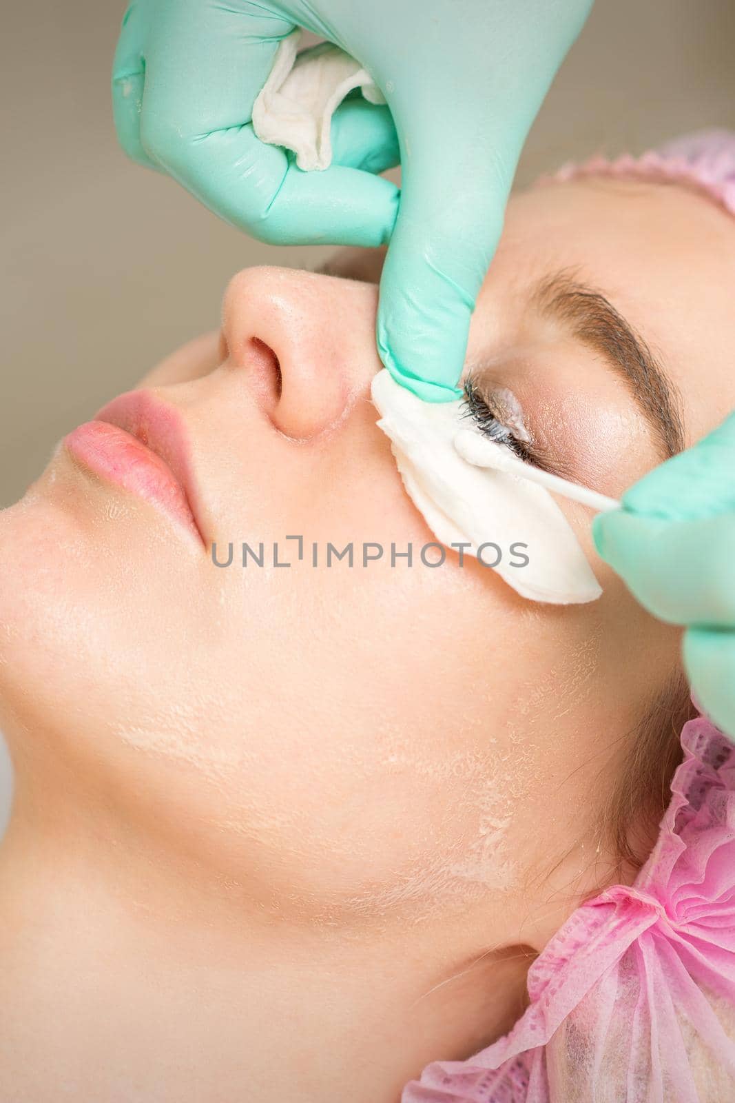 Young woman receiving eyelash removal procedure and removes mascara with a cotton swab and stick in a beauty salon