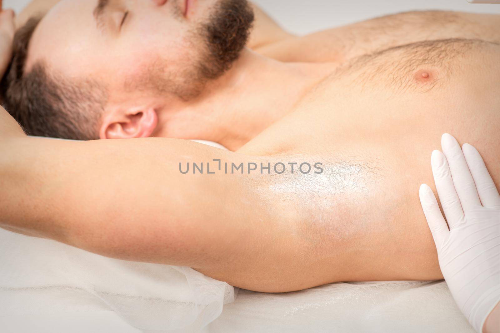 Young caucasian man receiving hair removal from his armpit in a beauty salon, depilation men's underarm