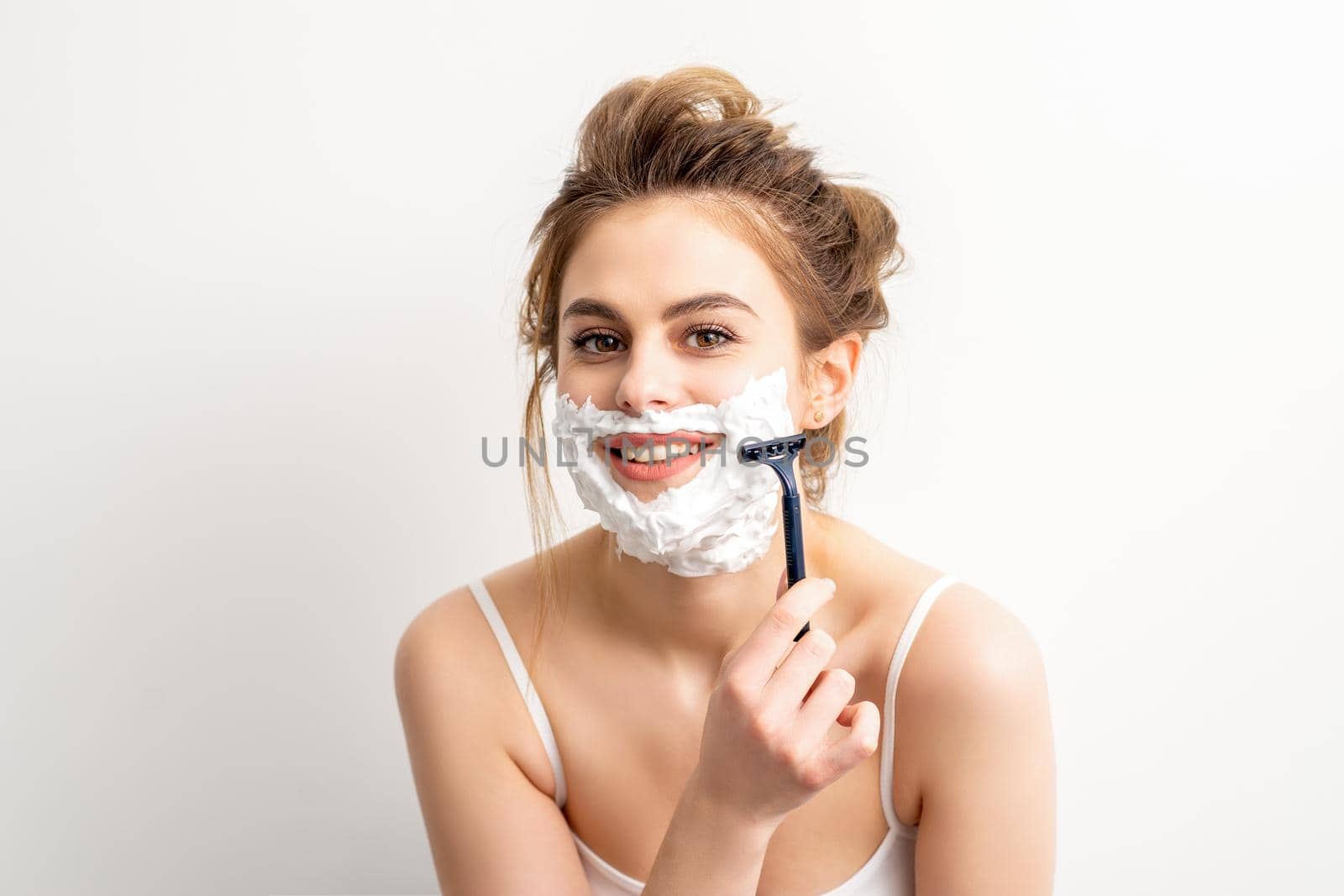 Portrait of beautiful young smiling caucasian woman shaves face with razor on white background